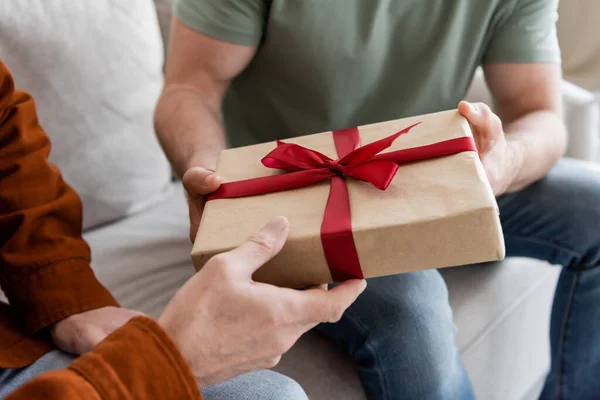 Partial view of man holding gift box with red ribbon while congratulating dad on fathers day — Stock Photo