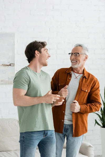 Happy young man talking with smiling mature father in eyeglasses at home — Stock Photo