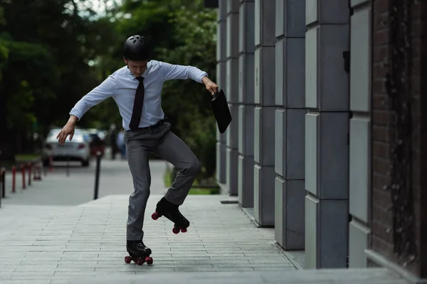 Смішний менеджер в шоломі і роликових ковзанах тримає портфель біля будівлі на міській вулиці — стокове фото