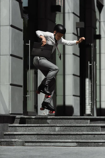 Jovem empresário de patins pulando e segurando pasta na rua urbana — Fotografia de Stock