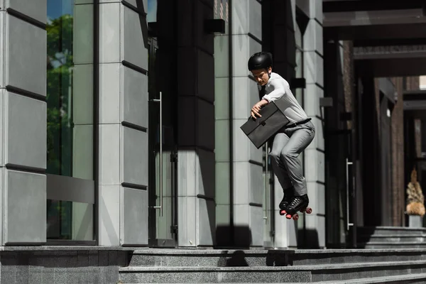 Бізнесмен в роликових ковзанах стрибає і тримає портфель під час їзди на міській вулиці — стокове фото