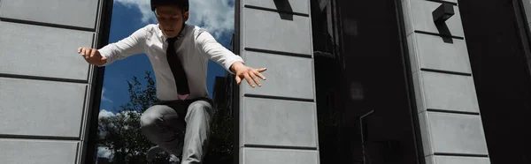 Empresario en casco y desgaste formal saltando cerca del edificio al aire libre, pancarta - foto de stock