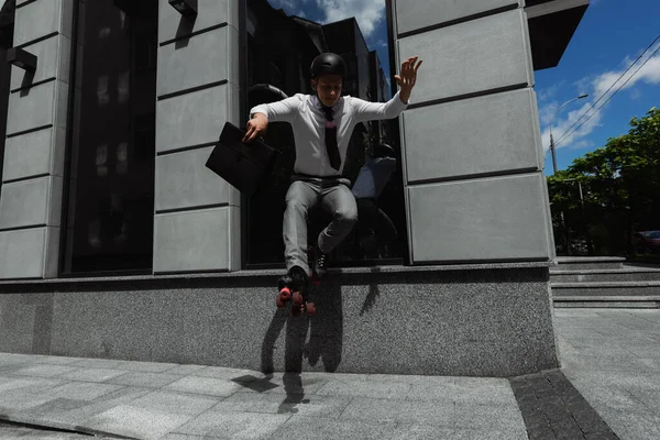 Молодой бизнесмен в роликовых коньках держит портфель и делает трюк на городской улице — стоковое фото
