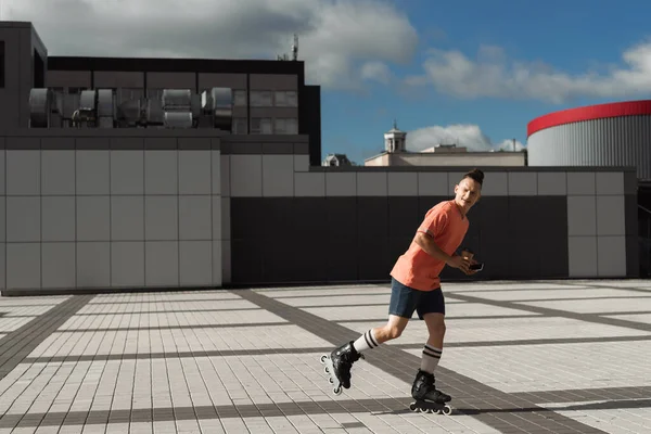 Молодий чоловік в роликових ковзанах тримає каву, щоб піти і смартфон під час їзди на міській вулиці — стокове фото