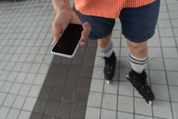 Обрізаний вид роликового ковзаняра, що тримає смартфон з порожнім екраном на відкритому повітрі — стокове фото