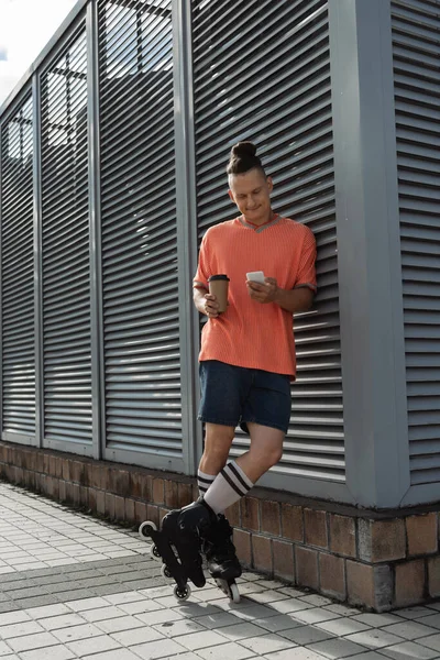 Позитивний роликовий ковзаняр тримає смартфон і каву на міській вулиці — стокове фото