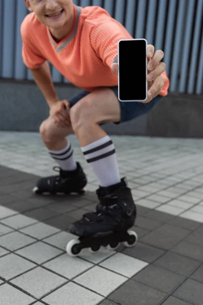 Vista ritagliata del pattinatore a rotelle sfocato che mostra smartphone con schermo vuoto sulla strada — Foto stock