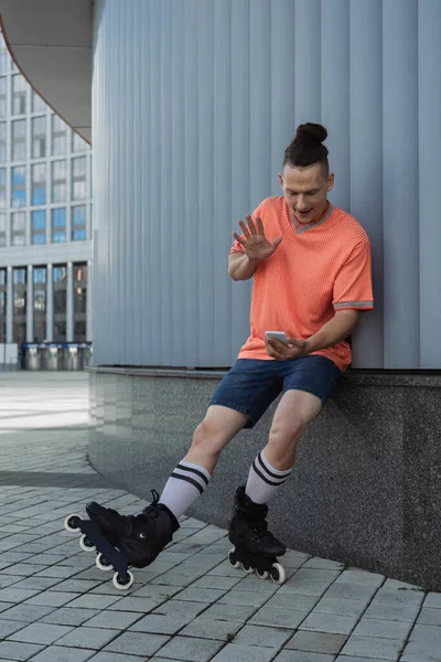 Roller skater in casual clothes having video call on smartphone near building outdoors — Stock Photo