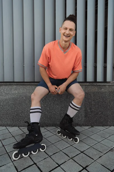 Веселый мужчина в повседневной одежде и роликовых коньках смотрит в камеру на городской улице — стоковое фото