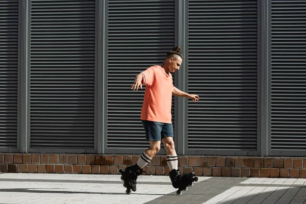 Вид сбоку на молодого человека в шортах и футболке, делающего трюк на роликовых коньках на открытом воздухе — стоковое фото