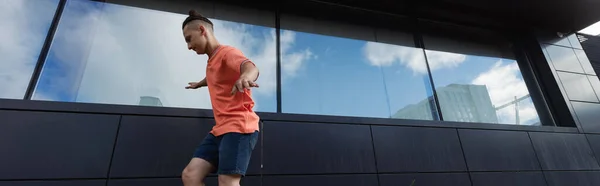 Side view of man in shorts and t-shirt walking near building outdoors, banner — Stock Photo