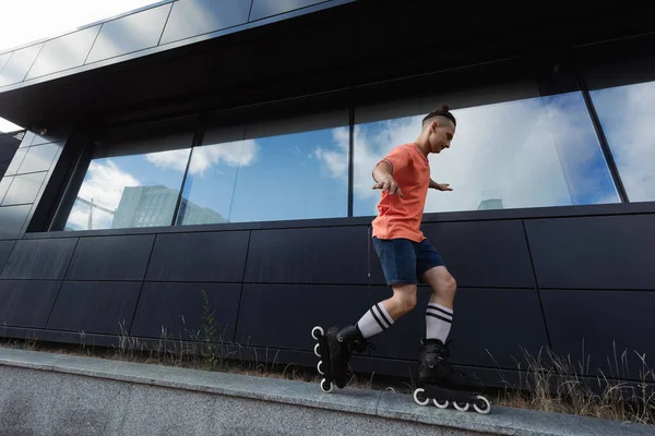 Vue latérale de l'homme en patins à roulettes faisant astuce sur parapet dans la rue urbaine — Photo de stock