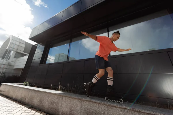 Молодой человек в роликовых клинках делает трюк на парапете возле здания на открытом воздухе — стоковое фото