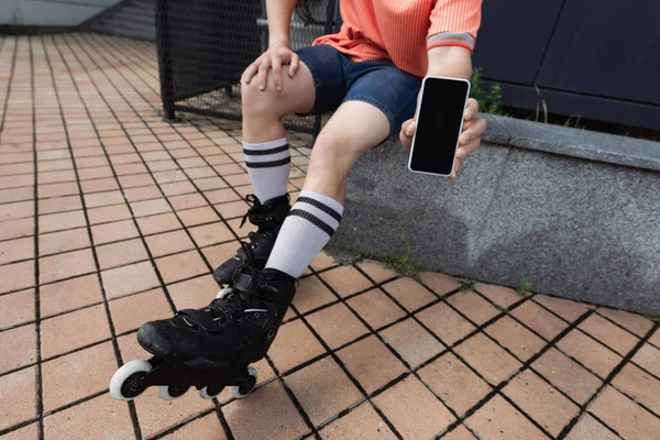 Vista recortada del hombre en rodillos y ropa casual que muestra el teléfono celular con pantalla en blanco al aire libre - foto de stock