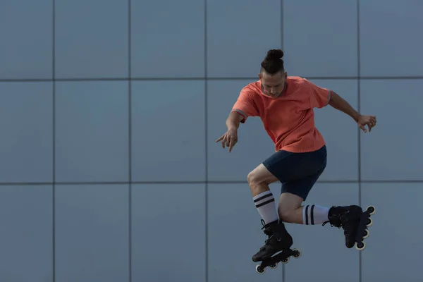 Молодий ковзаняр у шортах стрибає біля розмитої будівлі на відкритому повітрі — стокове фото