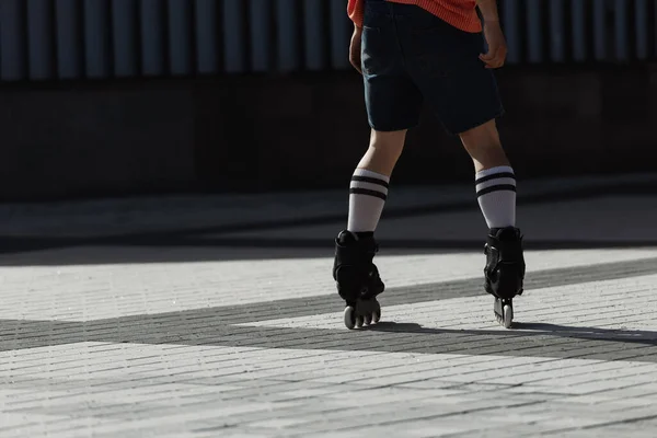 Vista recortada de un joven en pantalones cortos y patines de ruedas cabalgando en la plaza de la ciudad durante el día - foto de stock
