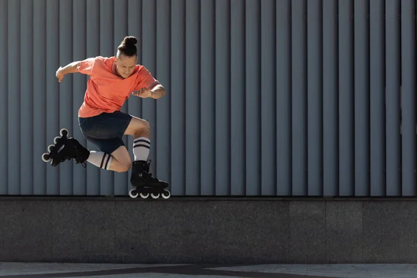 Человек в роликовых коньках прыгает во время тренировки возле здания на городской улице — стоковое фото