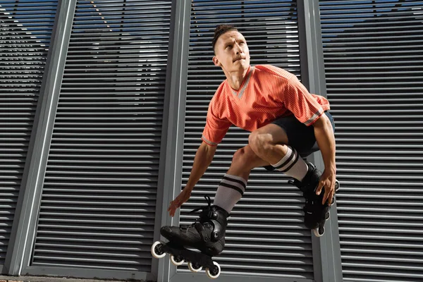 Hombre concentrado en calcetines y rodillos de rodilla saltando cerca del edificio en la calle urbana durante el día - foto de stock