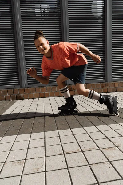 Uomo positivo guardando la fotocamera mentre pattinaggio a rotelle sulla strada urbana — Foto stock
