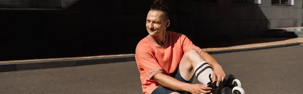 Hombre sonriente en camiseta y patines sentado en asfalto al aire libre, pancarta - foto de stock