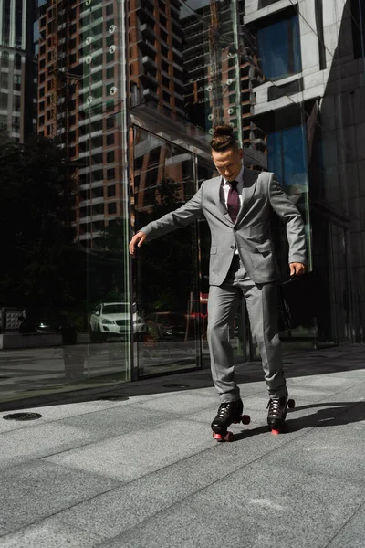 Full length of young businessman with trendy hairstyle roller skating on city street — Stock Photo