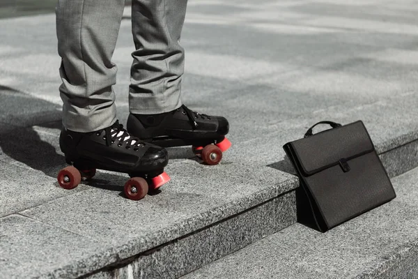 Частковий вид на бізнесмена в роликових ковзанах, що стоять біля чорного портфеля на міській вулиці — стокове фото