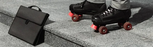Частичный взгляд бизнесмена в роликовых коньках возле черного портфеля на городской улице, баннер — стоковое фото