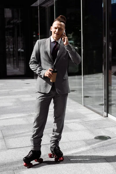 Homme d'affaires complet en costume et patins à roulettes tenant du café pour aller parler sur smartphone à l'extérieur — Photo de stock