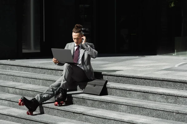 Geschäftsmann auf Rollschuhen stellt drahtlosen Kopfhörer ein, während er mit Laptop auf der Treppe sitzt — Stockfoto