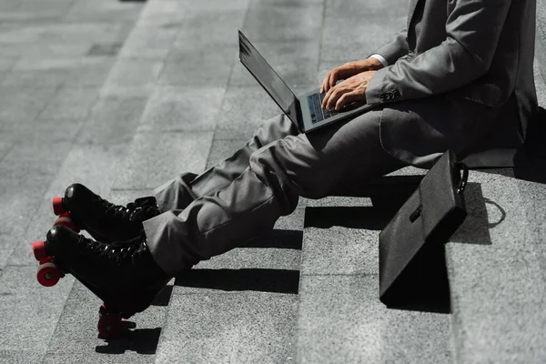 Partial view of roller skater in formal wear typing on laptop while sitting on stairs outdoors — Stock Photo