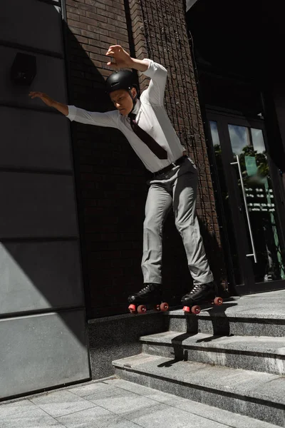 Toute la longueur du patineur à roulettes dans l'usure formelle et le casque sautant des escaliers sur la rue urbaine — Photo de stock