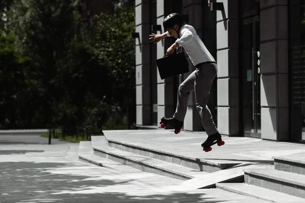 Vue latérale du patineur à roulettes en tenue formelle tenant la mallette et sautant des escaliers dans la rue — Photo de stock