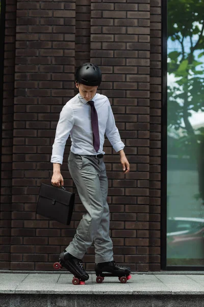 Full length of businessman in roller skates and protective helmet skating with briefcase on street — Stock Photo