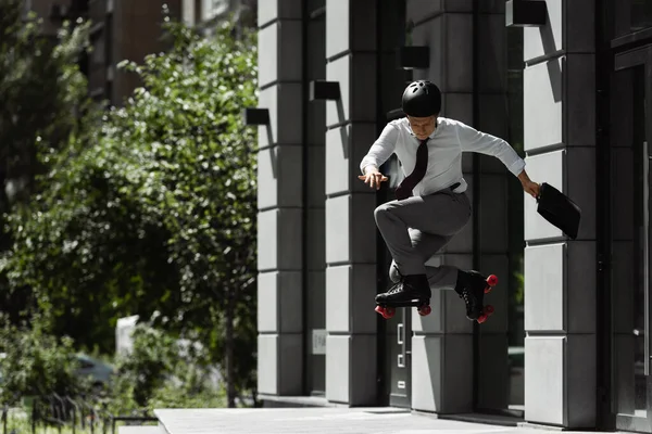 Повна довжина бізнесмена в роликових ковзанах і шоломі стрибає, роблячи трюк на вулиці біля будівлі — стокове фото