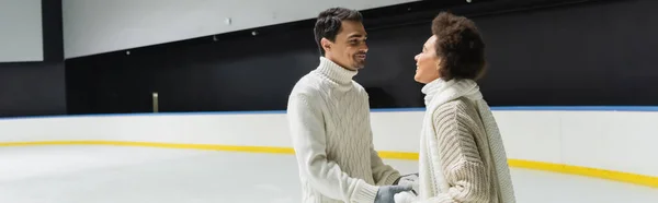 Cheerful interracial couple holding hands on ice rink, banner — Stock Photo