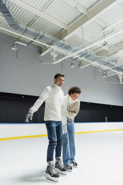 Femme afro-américaine souriante patinage sur glace avec petit ami sur la patinoire — Photo de stock