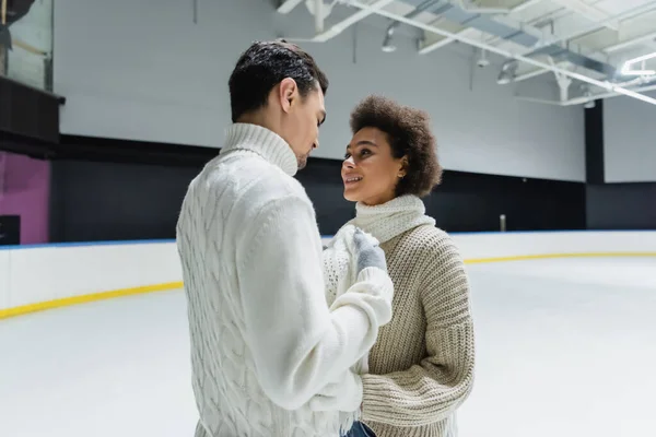 Young african american woman hugging boyfriend in knitted sweater on ice rink — Stock Photo