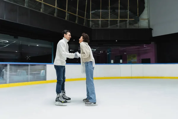 Side view of cheerful interracial couple spending time during date on ice rink — Stock Photo