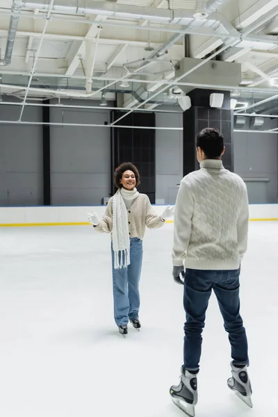 Souriante femme afro-américaine parlant à son petit ami en pull sur la patinoire — Photo de stock