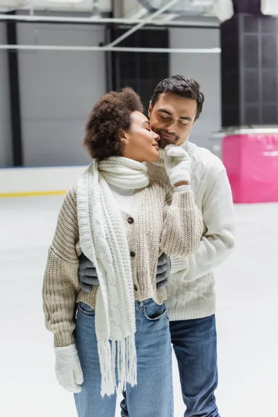 Man hugging african american girlfriend in warm clothes on ice rink — Stock Photo