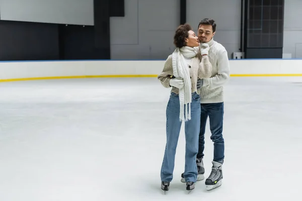Young african american woman kissing boyfriend in warm clothes on ice rink — Stock Photo