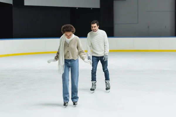 African american woman in scarf and gloves ice skating near boyfriend on rink — Stock Photo