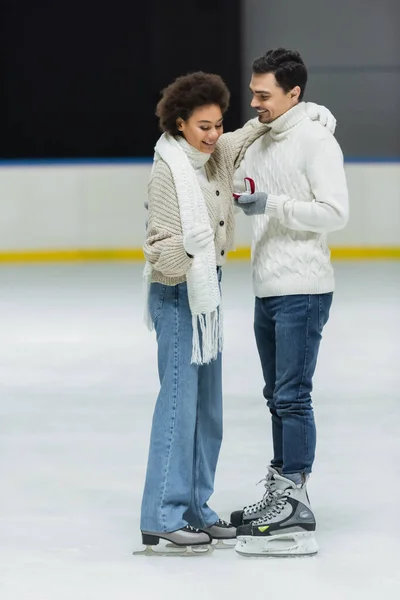Smiling african american woman looking at proposal ring near boyfriend on ice rink — Stock Photo