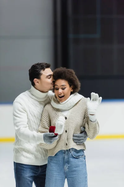 Excited african american woman looking at proposal ring in hand of boyfriend on ice rink — Stock Photo