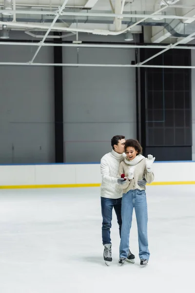 Homme étreignant petite amie afro-américaine et tenant la bague de fiançailles sur la patinoire — Photo de stock