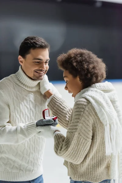 Excited african american woman touching boyfriend with proposal ring on ice rink — Stock Photo