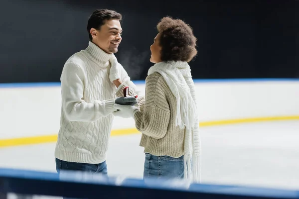 Un homme souriant tenant une bague de fiançailles et regardant une petite amie afro-américaine sur une patinoire — Photo de stock