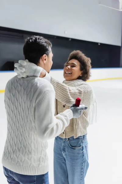 Happy african american woman hugging boyfriend with proposal ring on ice rink — Stock Photo