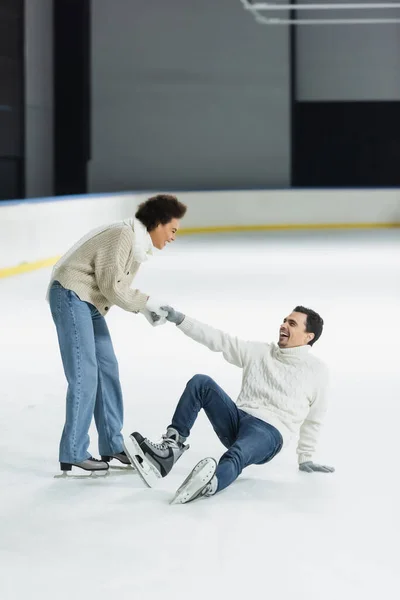 Cheerful african american woman holding hand of boyfriend on ice rink — Stock Photo