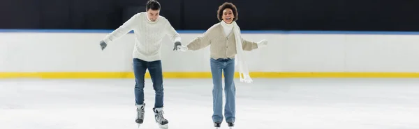 Весела міжрасова пара в теплих рукавичках катається на ковзанах, банер — стокове фото